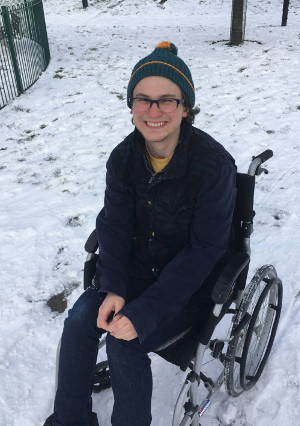 Kermie grinning from an iced‐up wheelchair, sinking in its own tracks through a snow‐covered park.